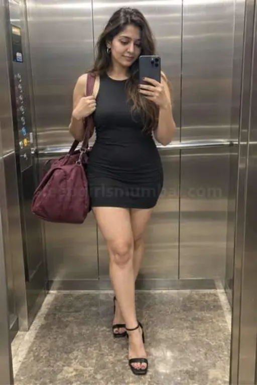 A woman in a short black dress taking a mirror selfie in a hotel lift with a maroon overnight bag